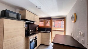 Una cocina compacta con armarios de madera, un microondas negro, una estufa y un lavamanos.
