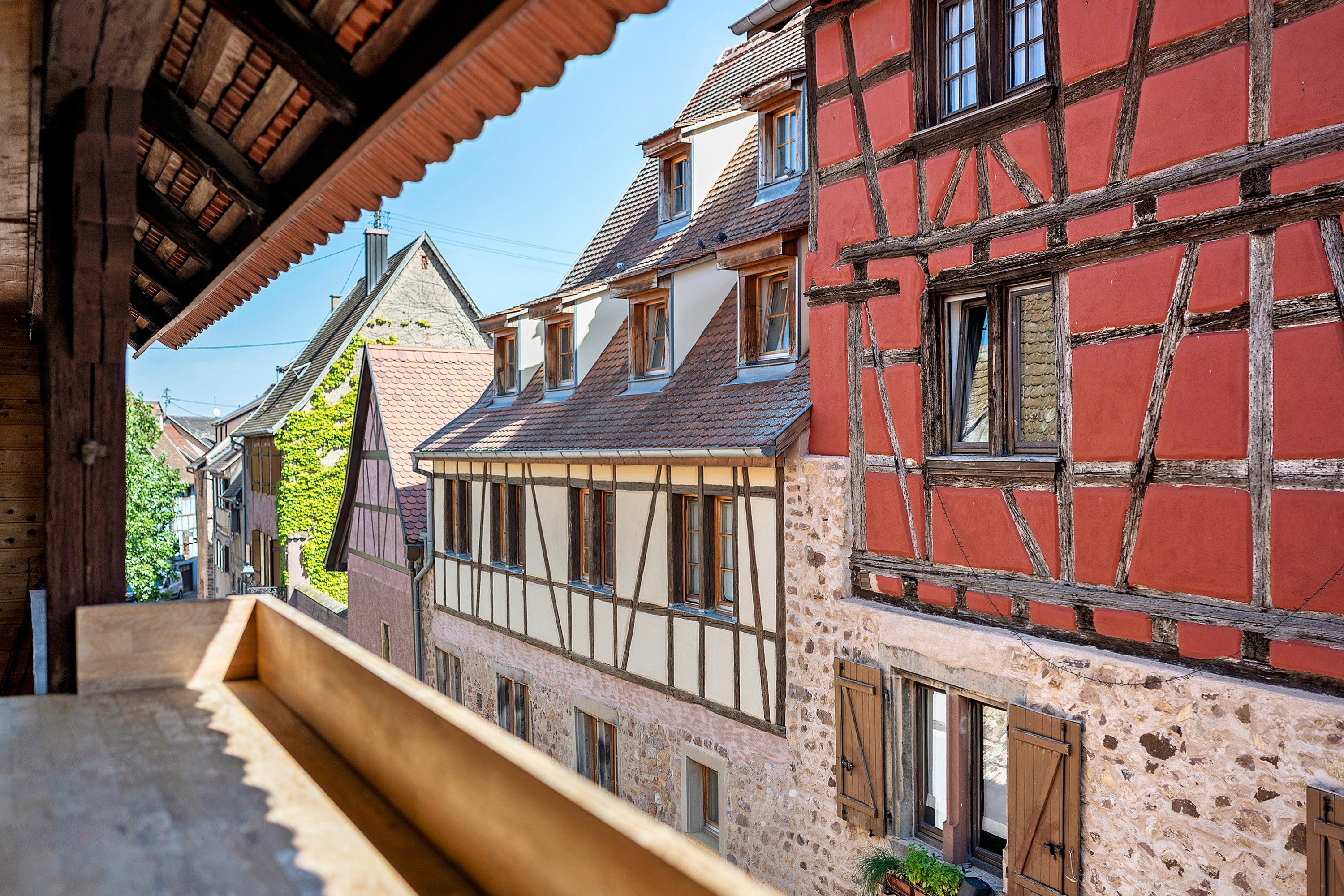 A narrow street with traditional half-timbered buildings, a wooden bench, and a clear sky.