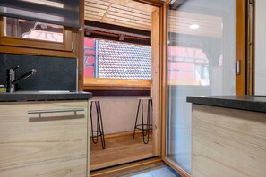Een keuken met houten kastjes, een roestvrijstalen spoelbak en een raam met uitzicht op een rood gebouw.