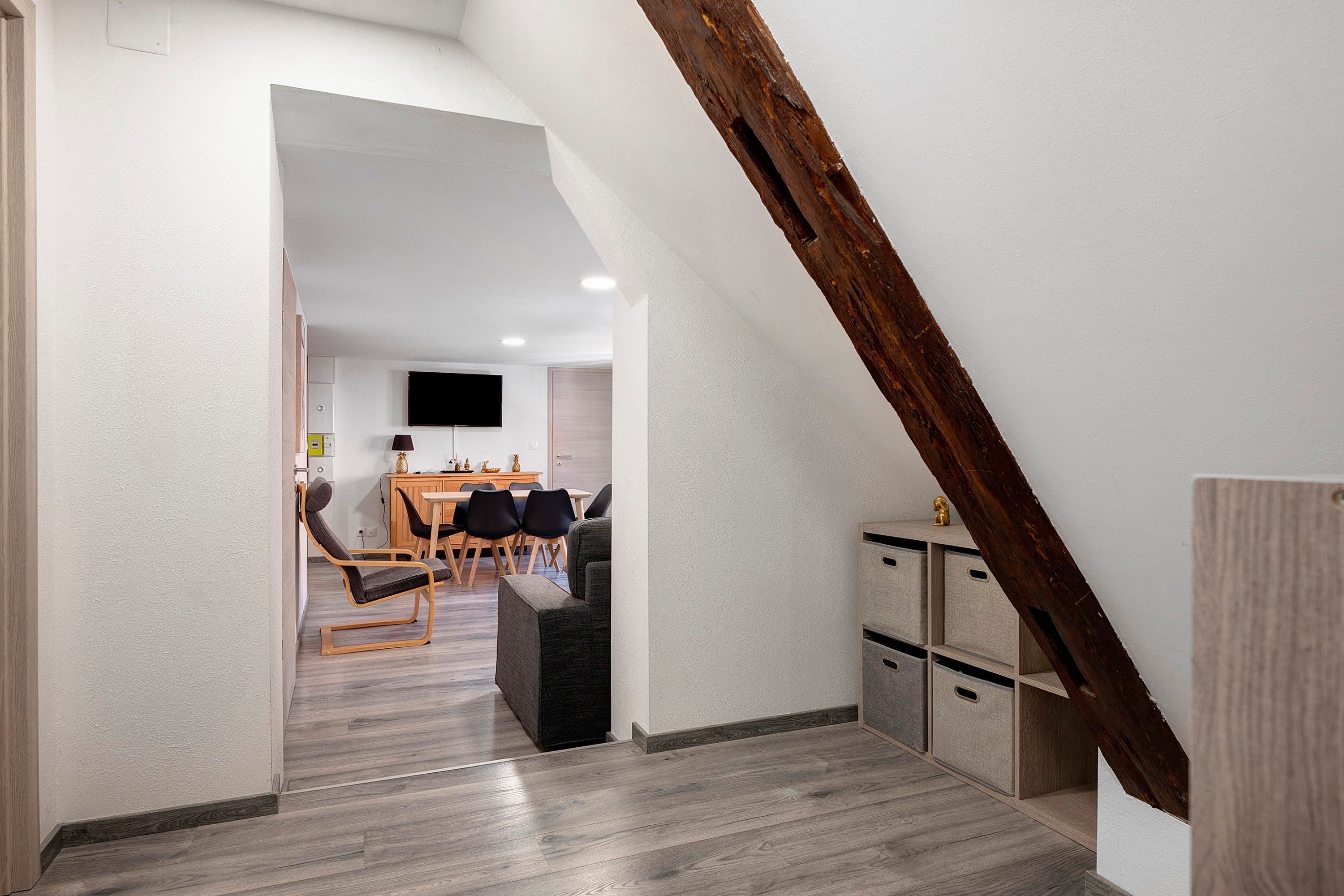 Ein modernes Interieur mit Essbereich, einem Wand-Fernseher und einem Schlafbereich mit Holzbalken.