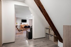 A modern interior with a dining area, a flat-screen TV mounted on the wall, and a loft space with wooden beams.
