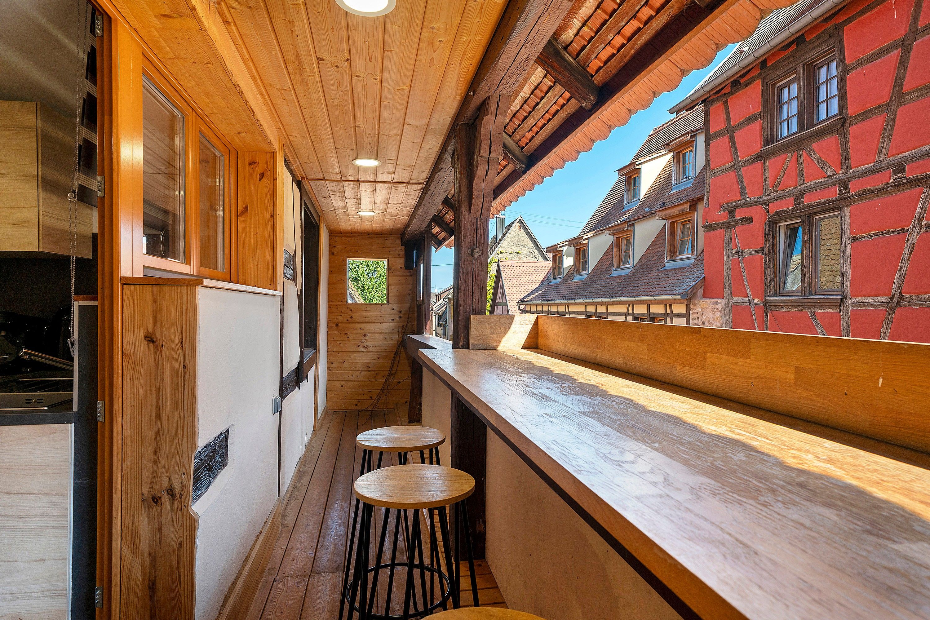 Un couloir étroit aux murs et au plafond en bois, qui mène à un espace bar équipé de tabourets.