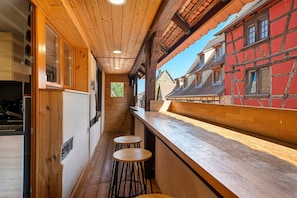 A narrow corridor with wooden walls and a wooden ceiling, leading to a bar area with stools.
