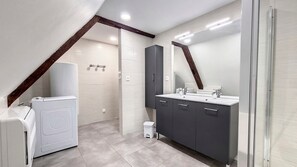 Un baño moderno con lavadora integrada, un mueble de tocador oscuro con espejo y zona de ducha.