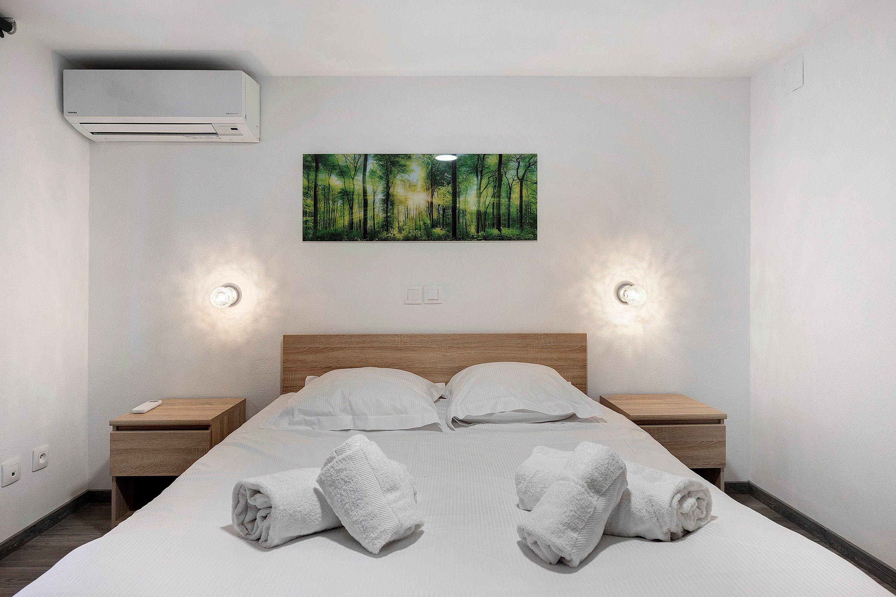 Une chambre d’hôtel comprenant un lit, deux tables de chevet, un appareil de climatisation et une décoration murale sur le thème de la forêt.
