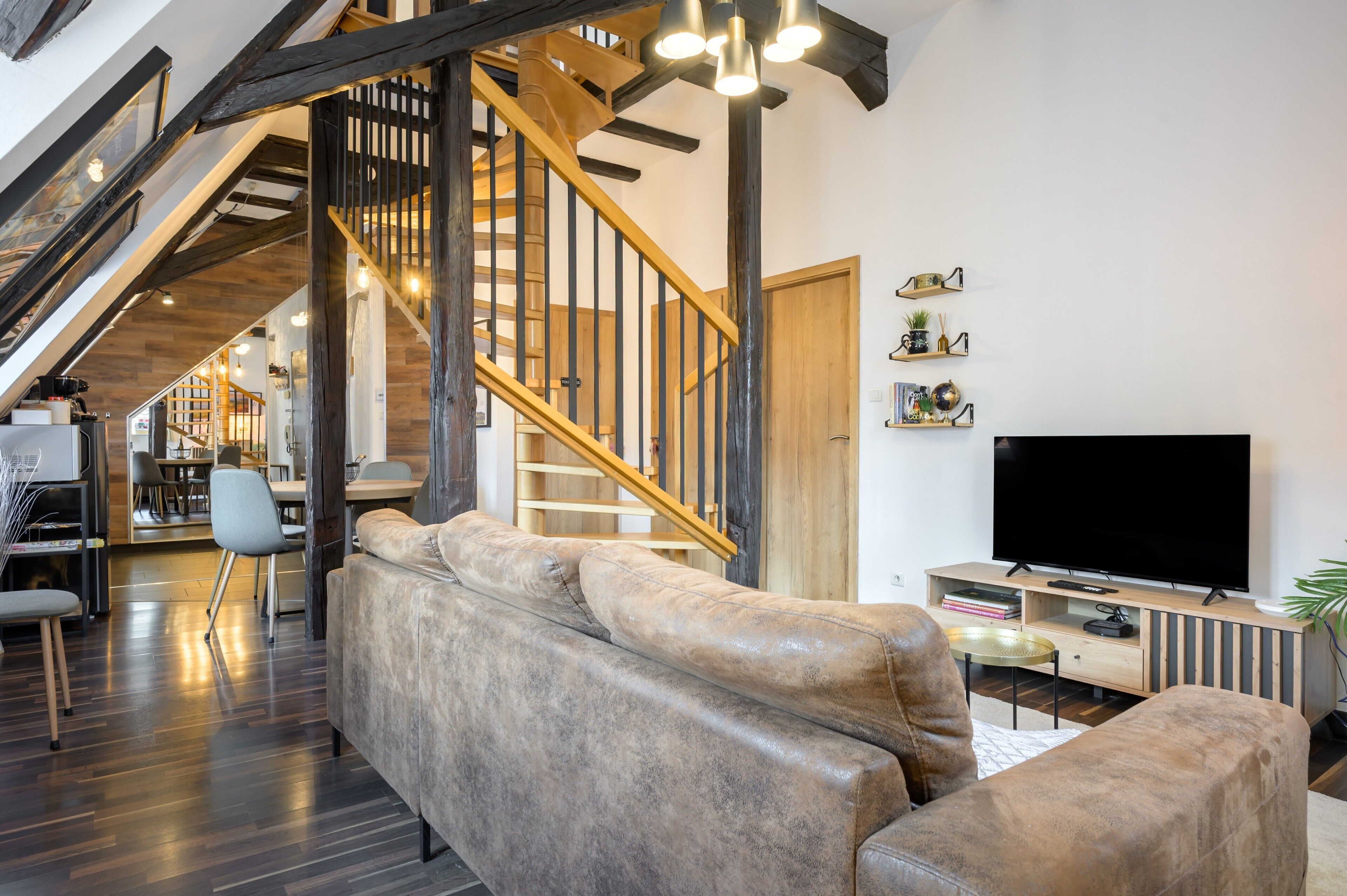 A modern living room with a staircase, a large flat-screen TV, and a sofa.