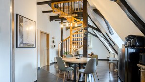 A modern interior with a wooden staircase, a dining area with a round table and chairs, and a kitchen area with a black refrigerator. - Loft Bariga Apartment – Between Vineyards and Ramparts (Bergheim)