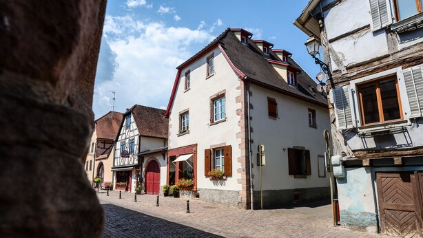 A cobblestone street lined with traditional European buildings, featuring a mix of architectural styles and a clear blue sky. - Loft Bariga Apartment – Between Vineyards and Ramparts (Bergheim)