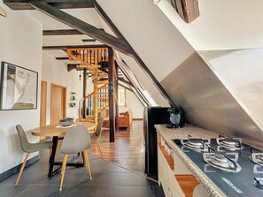Uma cozinha moderna com fogão a gás, mesa de jantar de madeira e cadeiras. Uma escada em espiral leva a um andar superior.