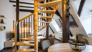 A wooden spiral staircase in a room with a round wooden table, a bottle of wine, and a bookshelf. - Loft Bariga Apartment – Between Vineyards and Ramparts (Bergheim)