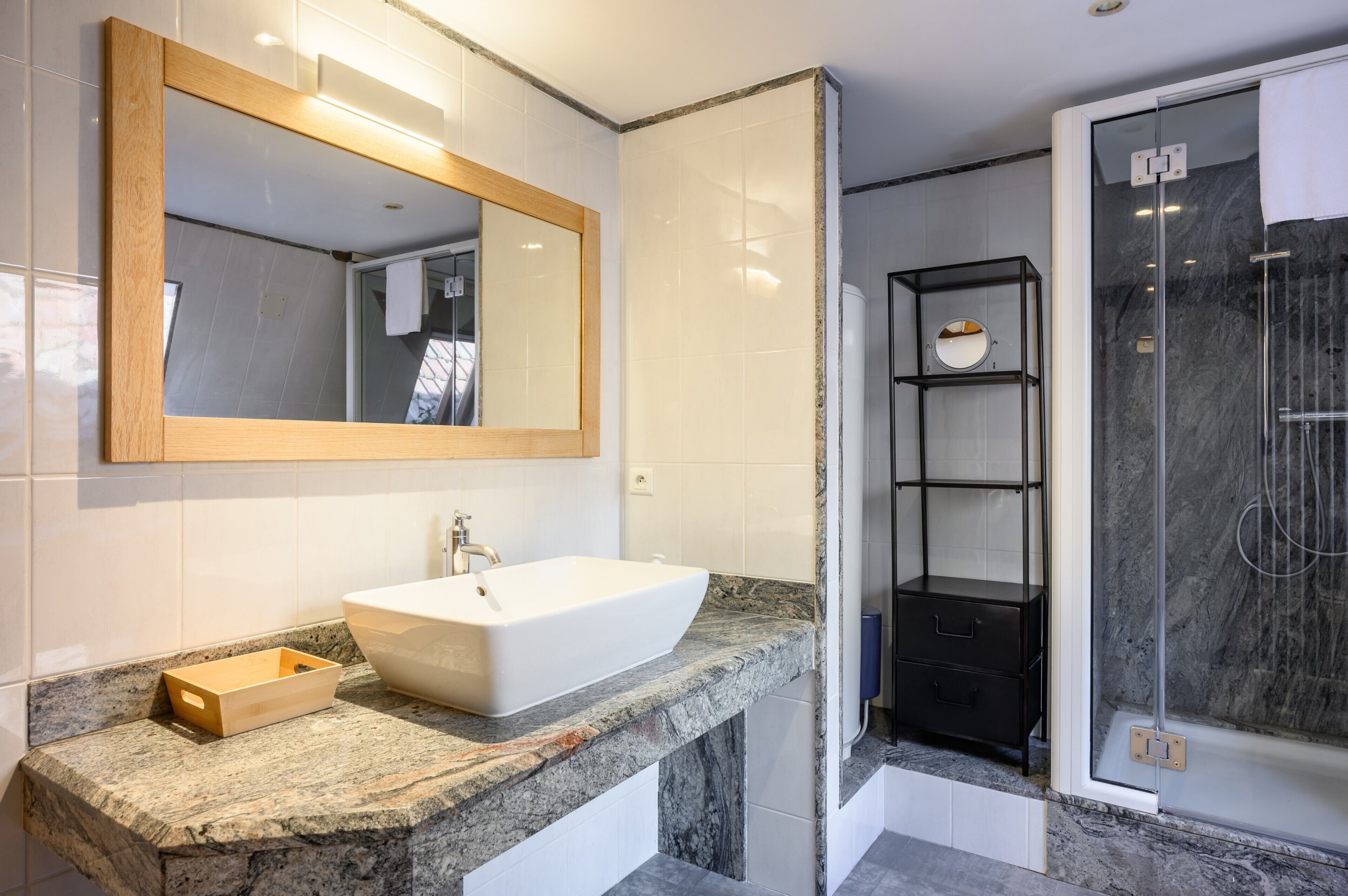 A modern bathroom with a large mirror, a white sink, a shower enclosure, and a marble countertop.