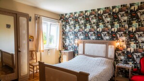 Un dormitorio con cama, una silla, una mesita, un espejo y una ventana con cortinas.