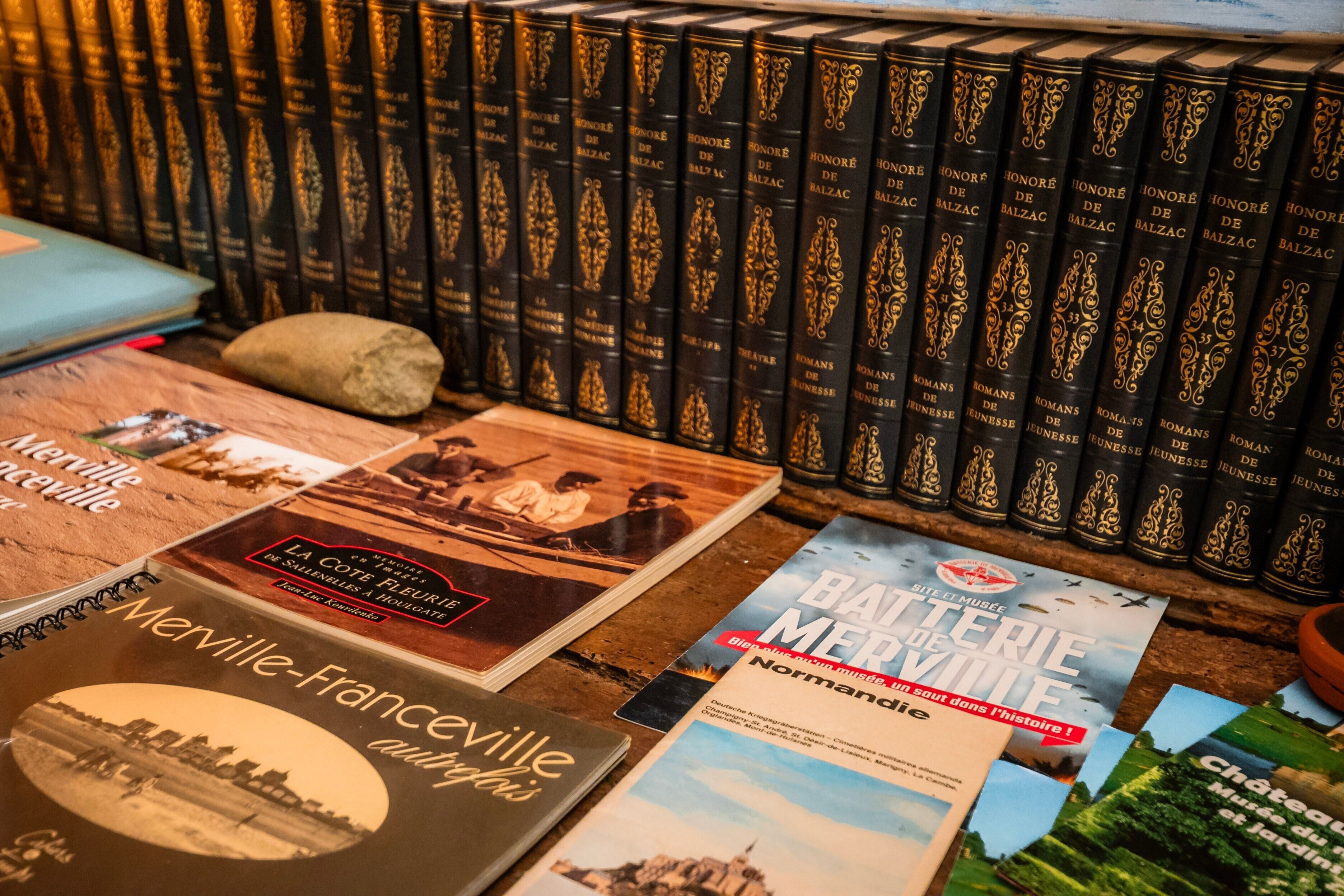 Een verzameling boeken, waaronder 'La Côte Fleurie' en 'Batterie Musee Normandie,' op een houten oppervlak.
