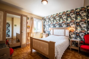 Une chambre à coucher comprenant un lit, une chaise, une petite table, un miroir et une porte donnant sur une autre pièce.