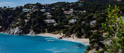 A coastal landscape with houses on a hillside, a beach, and a view of the sea.