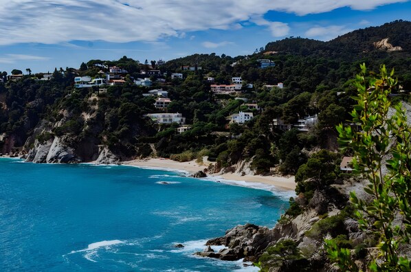 A coastal landscape with houses on a hillside, a beach, and a view of the sea.