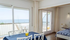 Ett rum med en balkong, en säng, ett bord med stolar och utsikt över havet.