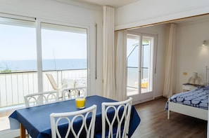 Ein Zimmer mit Balkon, einem Bett, einem Tisch mit Stühlen und Meerblick.