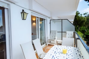 Uma varanda com mesa, cadeiras, um vão de vidro e uma luminária.