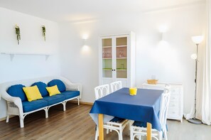 Ein Zimmer mit einer weißen Couch, blauen Kissen, einem Tisch mit blauer Tischdecke und einem Schrank mit Glastüren.