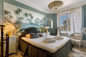 A bedroom with a large bed, a nightstand, a chair, a window with curtains, and a wall mural. - Holiday Home 'L'écrin Provençal' with Private Pool, Private Terrace and Wi-Fi (Callian)