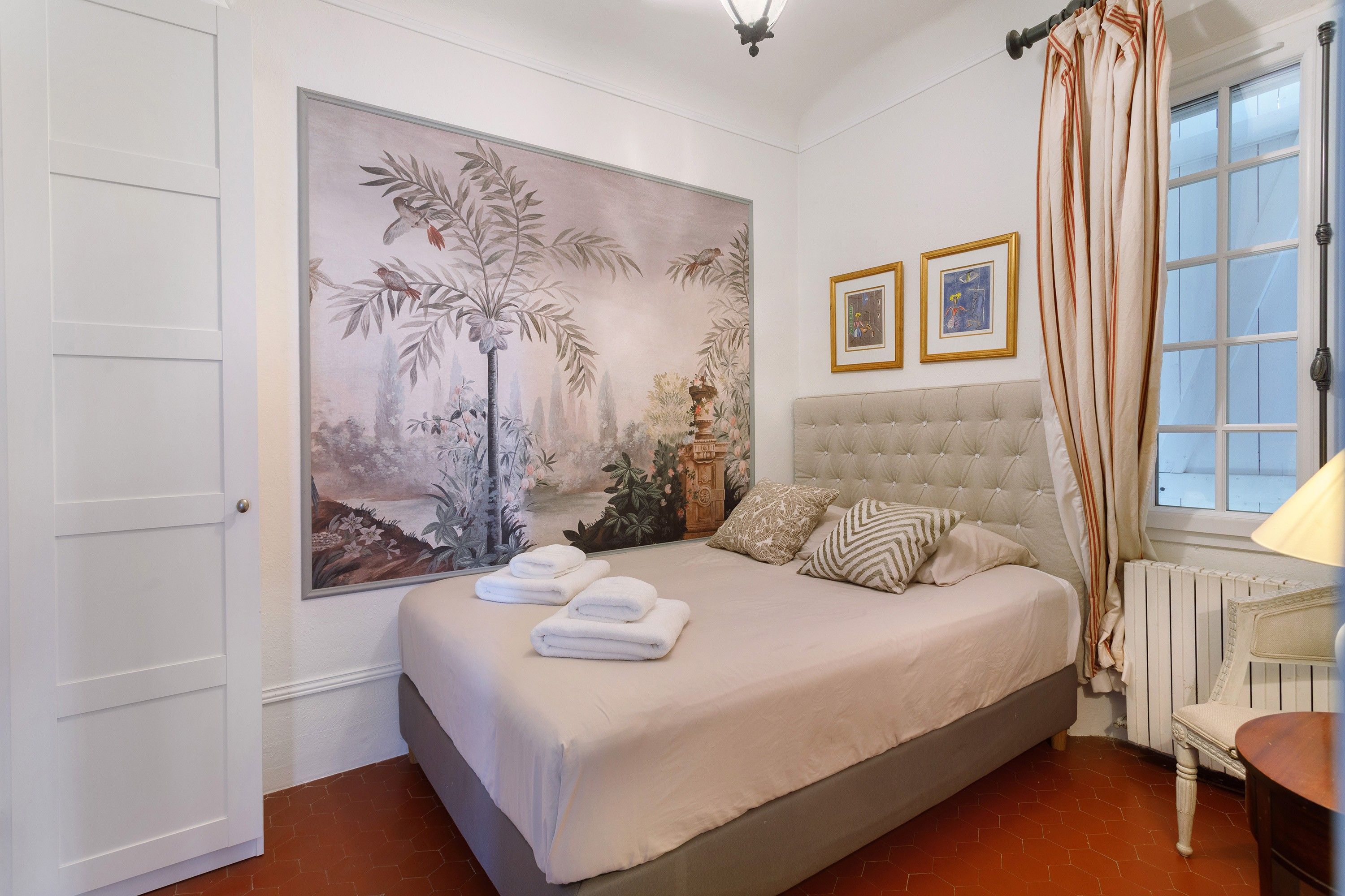 Un dormitorio con una cama grande, una ventana con cortinas, un radiador y una pared con un cuadro grande.