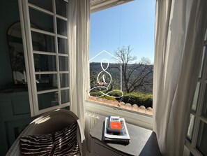 Una habitación con ventana que da a un paisaje, un radiador, una silla y una mesa con un libro.