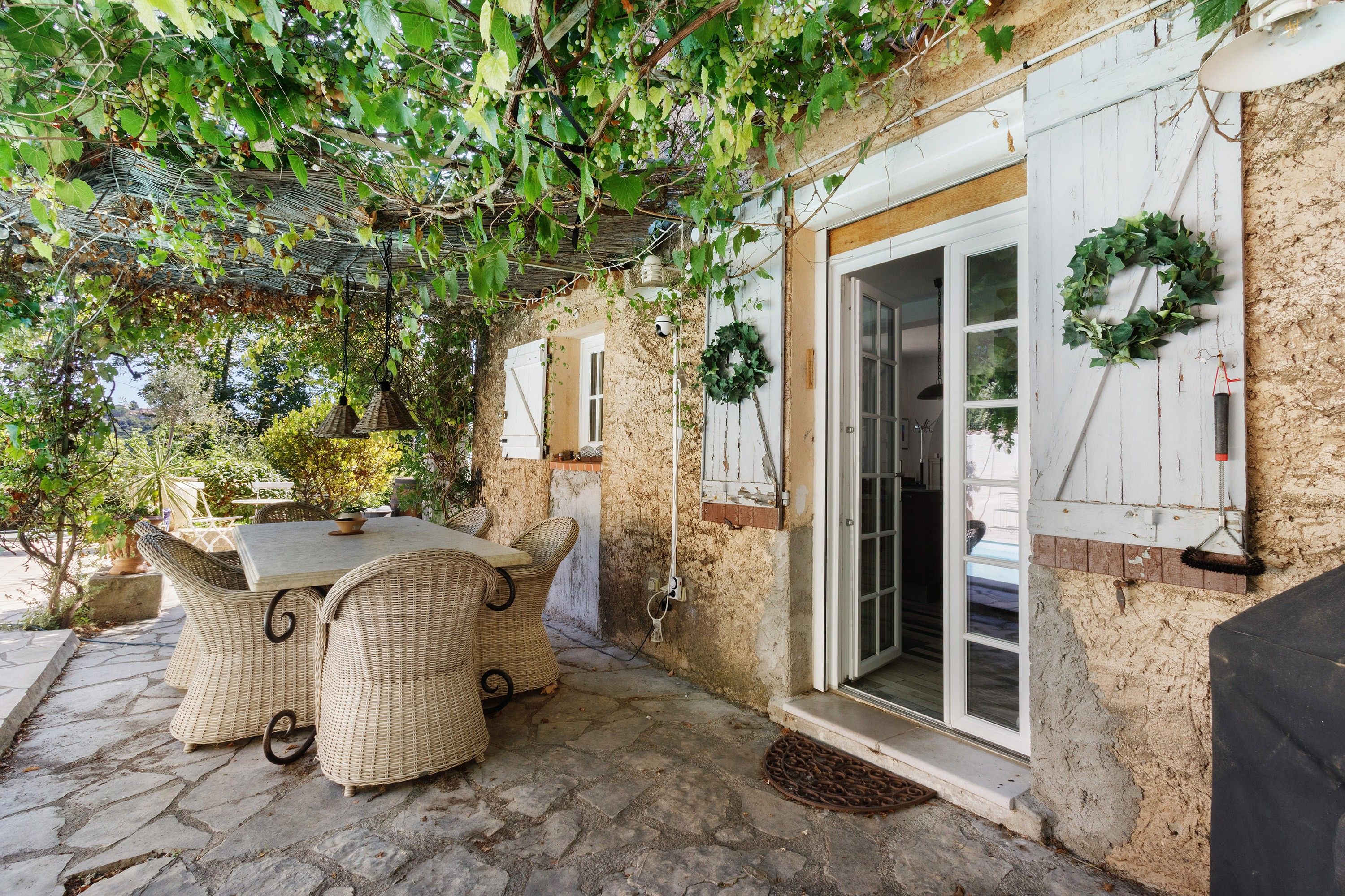 A covered outdoor seating area with wicker furniture, a stone floor, and a building entrance with a door and window.