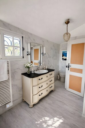 Un baño con pared de mármol, tocador doble, espejo, candelabro y puerta con vistas al exterior.