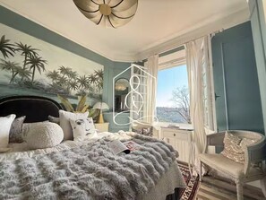 Ein Schlafzimmer mit Bett, Stuhl, Fenster und Wandgemälde.
