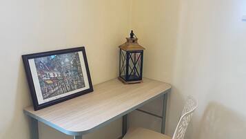Une pièce d’angle avec un tableau encadré posé sur un bureau de couleur claire, une petite lanterne et une chaise blanche.