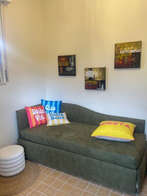 A green sofa with colorful pillows, a small round stool, and three wall-mounted artworks. - Villa Mario – Private Hot Tub and Mountain View in Rosciano (Rosciano)