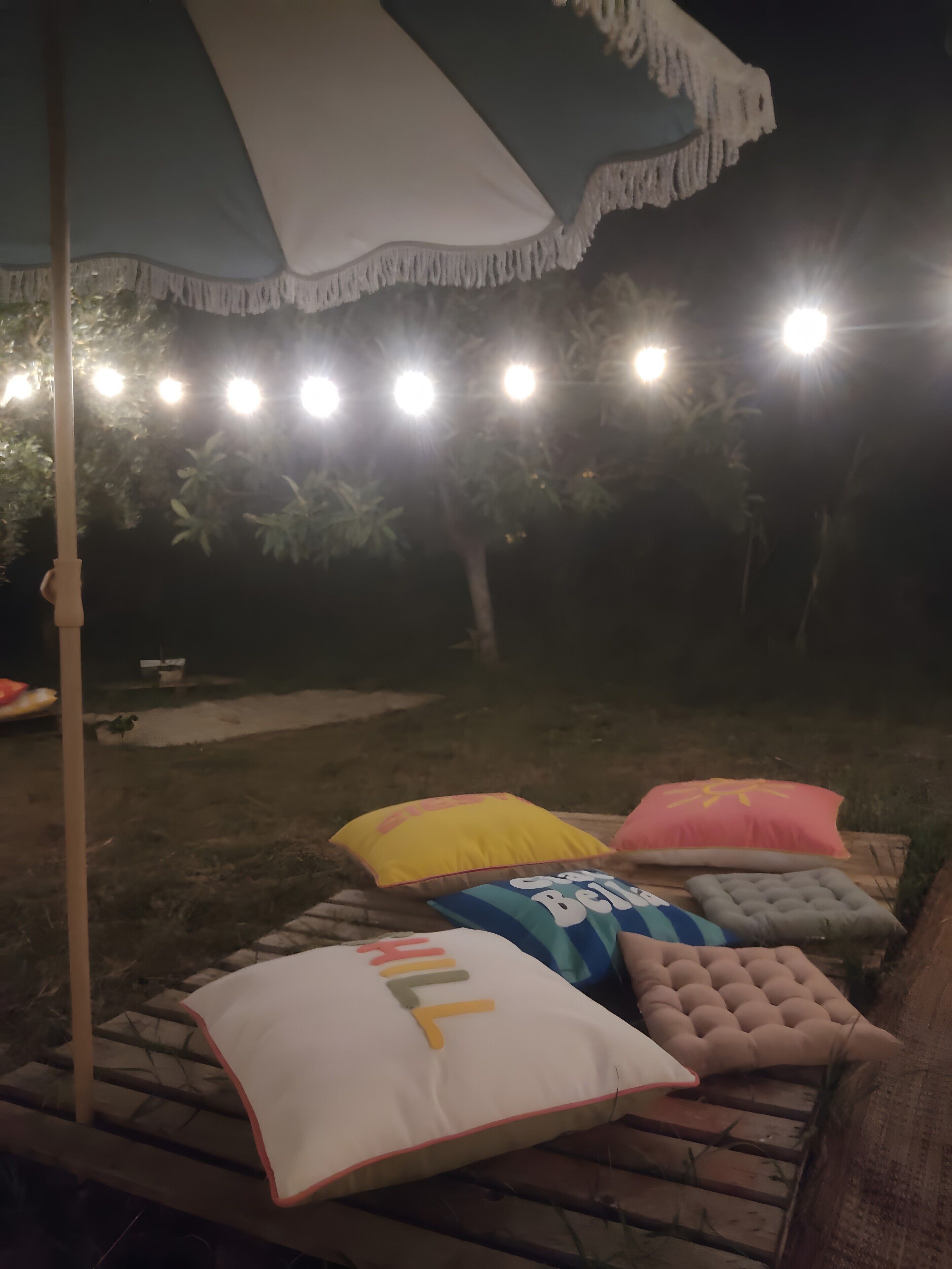 A patio area with a bench, pillows, and a hanging umbrella.