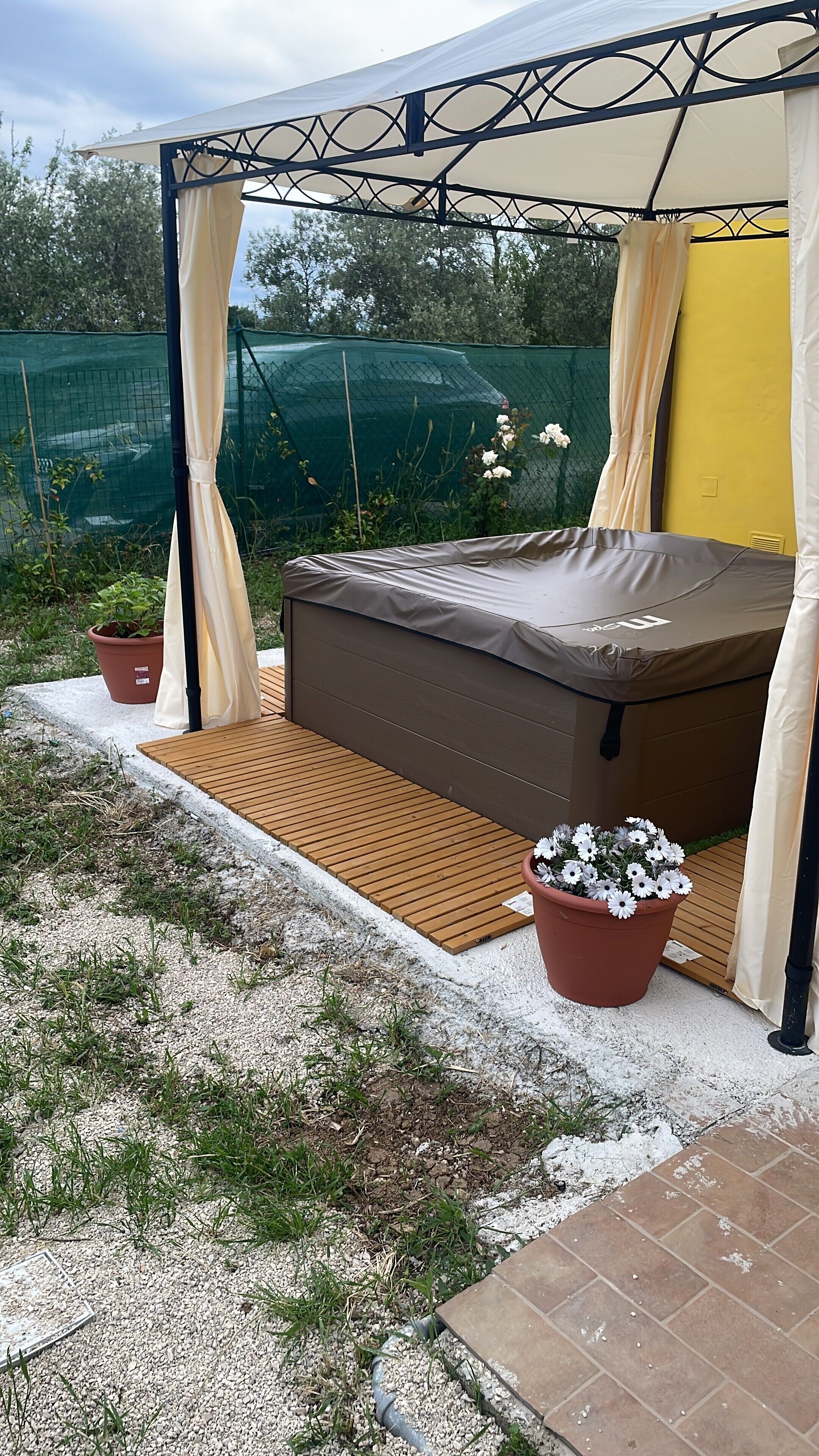 A tented outdoor area with a bed, potted plants, and a gravel path.