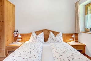 A bedroom with a wooden headboard, two beds with floral bedding, bedside lamps, a wooden wardrobe, and a window with a curtain. - Apartment 'Morgenrot' with Mountain View, Shared Terrace and Wi-Fi (Ritten)