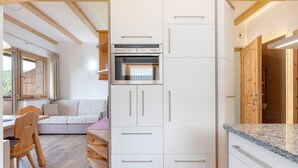 A compact kitchen with built-in appliances, a dining area with a wooden table and chairs, and a window with curtains. - Apartment “Morgenrot” with Mountain View, Shared Terrace, and Wi-Fi (Ritten)