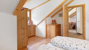 A bedroom with a sloped ceiling, wooden furniture, and a bed with floral bedding. - Apartment “Morgenrot” with Mountain View, Shared Terrace, and Wi-Fi (Ritten)