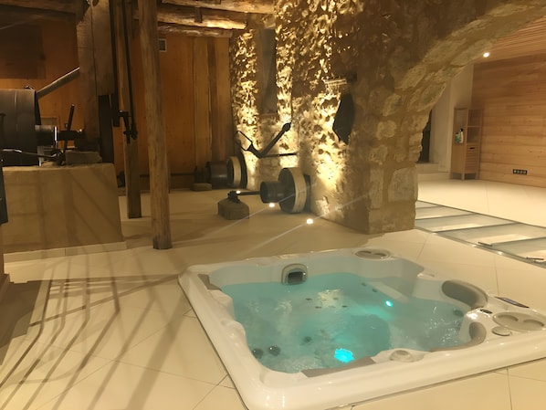A spa area with a hot tub, wooden beams, stone walls, and a tiled floor.