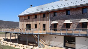 A two-story building with a wooden exterior, a metal roof, and a covered outdoor area with stairs. - Gîte De La Scie: vacation home with mountain views, private terrace, and Wi-Fi (Les Rousses)