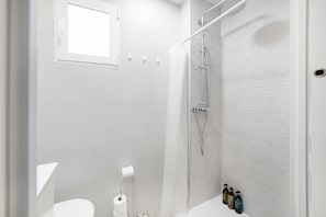 Ein modernes Duschbad mit Glastür, Toilette und einer kleinen Fensterfläche.