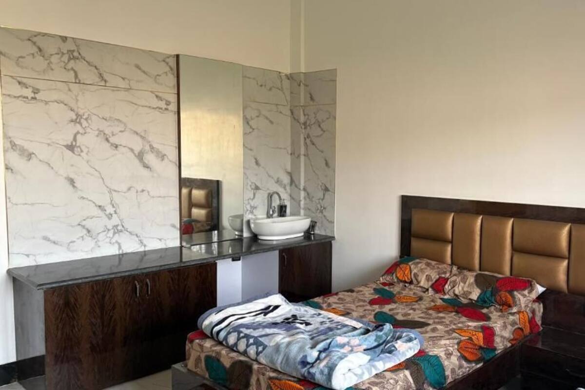 Una habitación de hotel con pared de mármol, una cama con cubrecama estampado, una mesita de noche y un espejo grande.