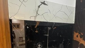 A bathroom with a white sink, black and white marble backsplash, a blue bucket, and a shower area. - Shree Laxmi Banquet & Hotel (Darbhanga)