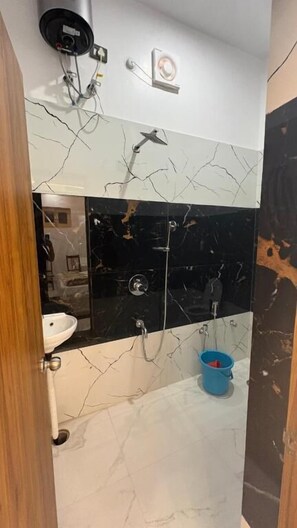 Ein Badezimmer mit einem weißen Waschbecken, einer schwarz-weißen Marmor-Spritzschutzleiste, einem blauen Eimer und einer Duschkabine.