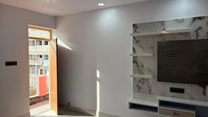 Un salon moderne doté d’un grand téléviseur à écran plat, d’étagères murales à motifs de marbre et d’une porte donnant sur un espace extérieur.