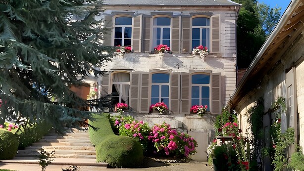 Un edificio de dos pisos con fachada de piedra, varias ventanas y una chimenea.