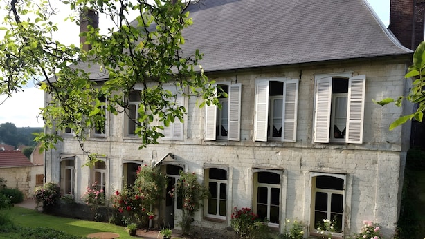 A stone building with multiple windows and shutters, surrounded by a well-maintained garden with various plants and flowers.