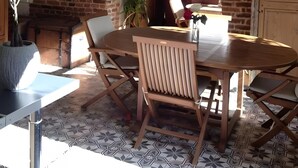 A dining area with a brick wall, wooden table, chairs, and a potted plant.