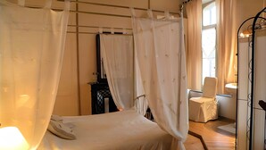 A bedroom with a canopy bed, a bedside table, a chair, and a mirror.