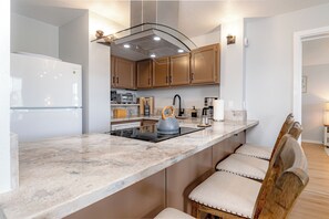 A modern kitchen with a marble countertop, wooden cabinets, a kettle, and a built-in stove.