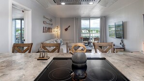 Een moderne keuken met een zwart inductiefornuis, houten stoelen en een groot raam met uitzicht over de stad.
